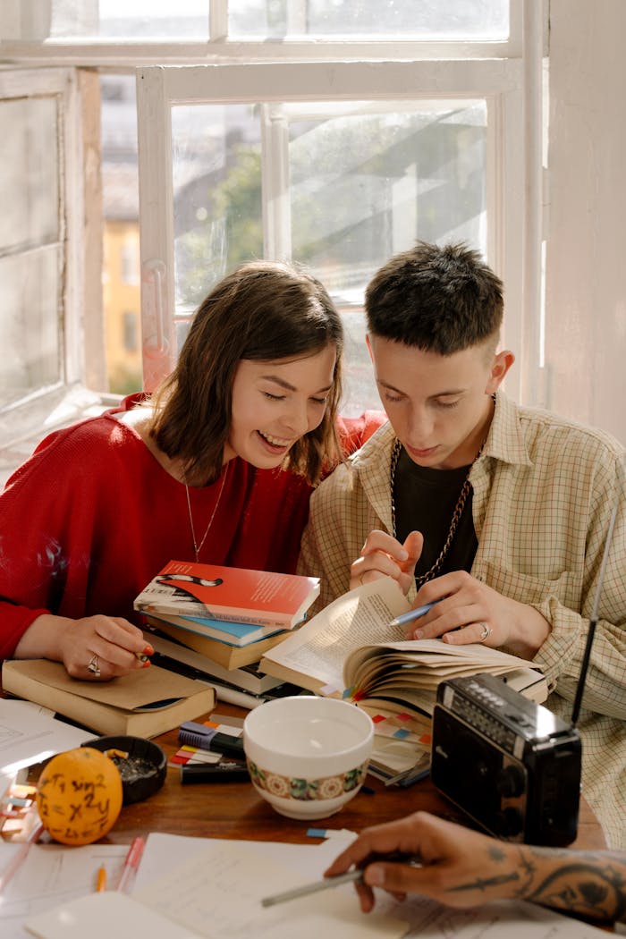Two young adults study together with textbooks at a table, surrounded by notes and stationery.